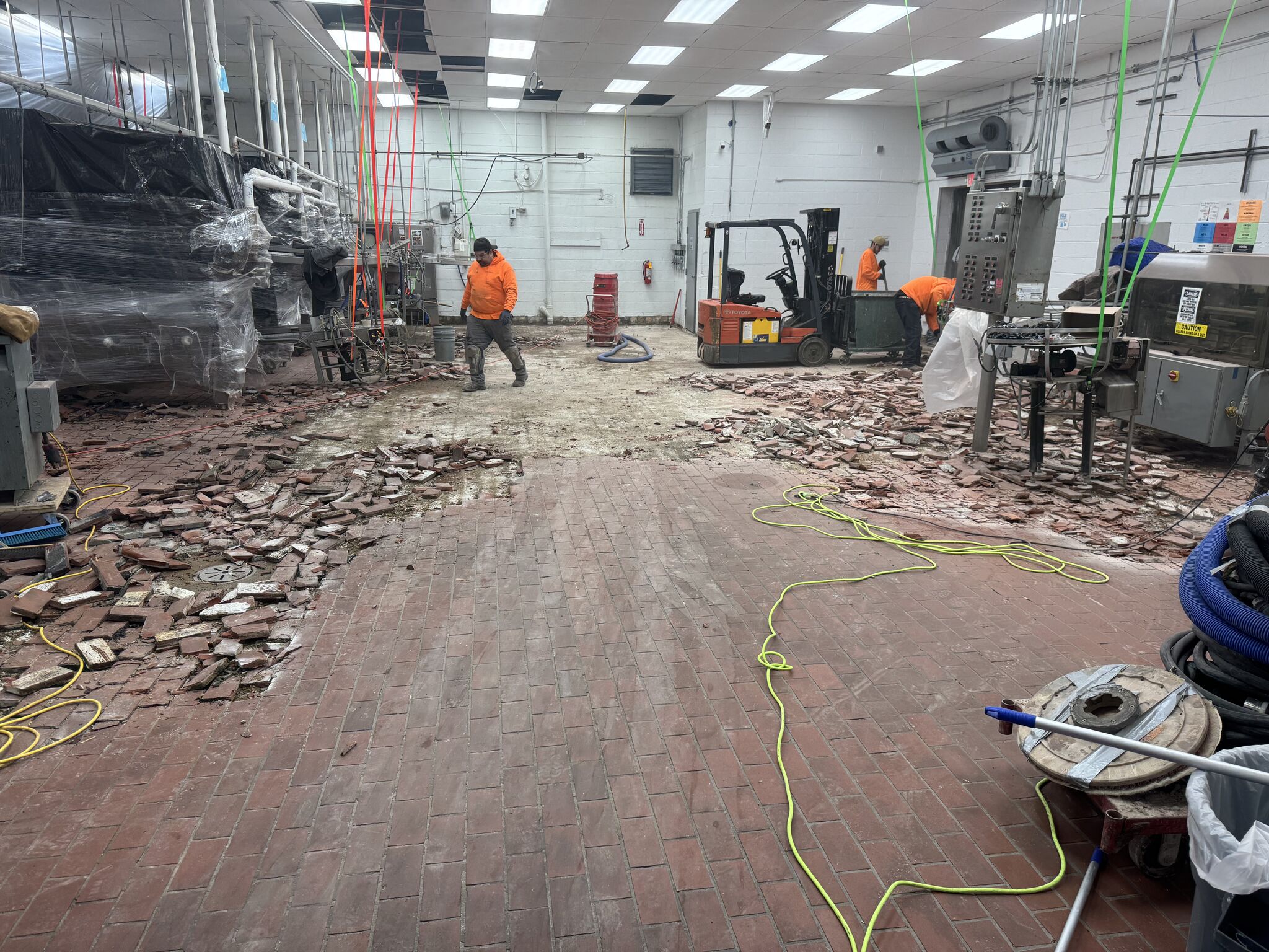 SaniCrete crew removing failing dairy brick from production floor with forklift and chipping tools at dairy processing facility