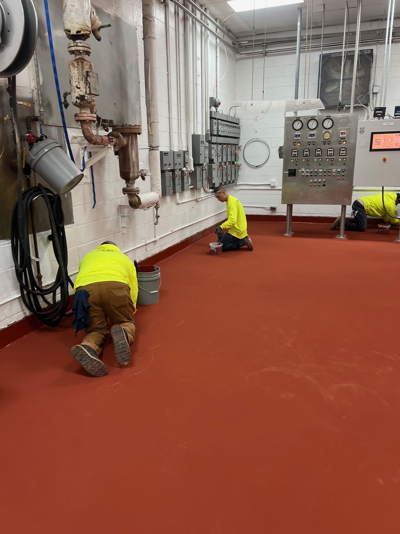 SaniCrete crew installing radius cove base in dairy facility with completed red SL floor