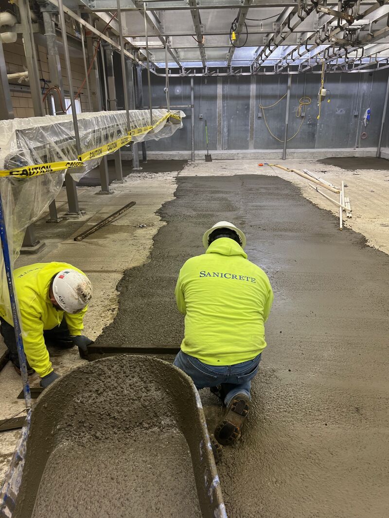 SaniCrete crew members troweling cementitious urethane floor with proper slope to drains in food processing facility