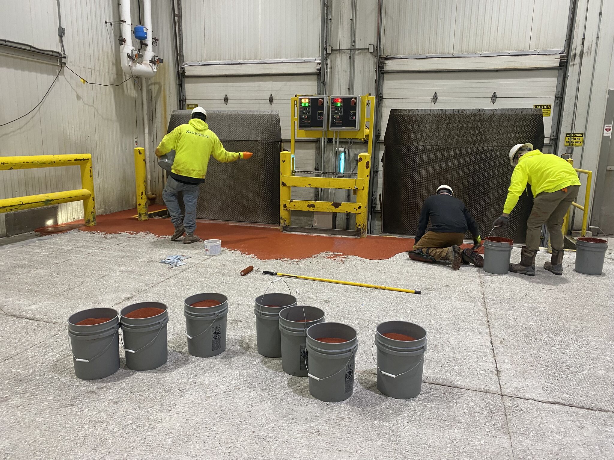 SaniCrete crew applying resinous coating to loading dock walls and floor around dock leveler