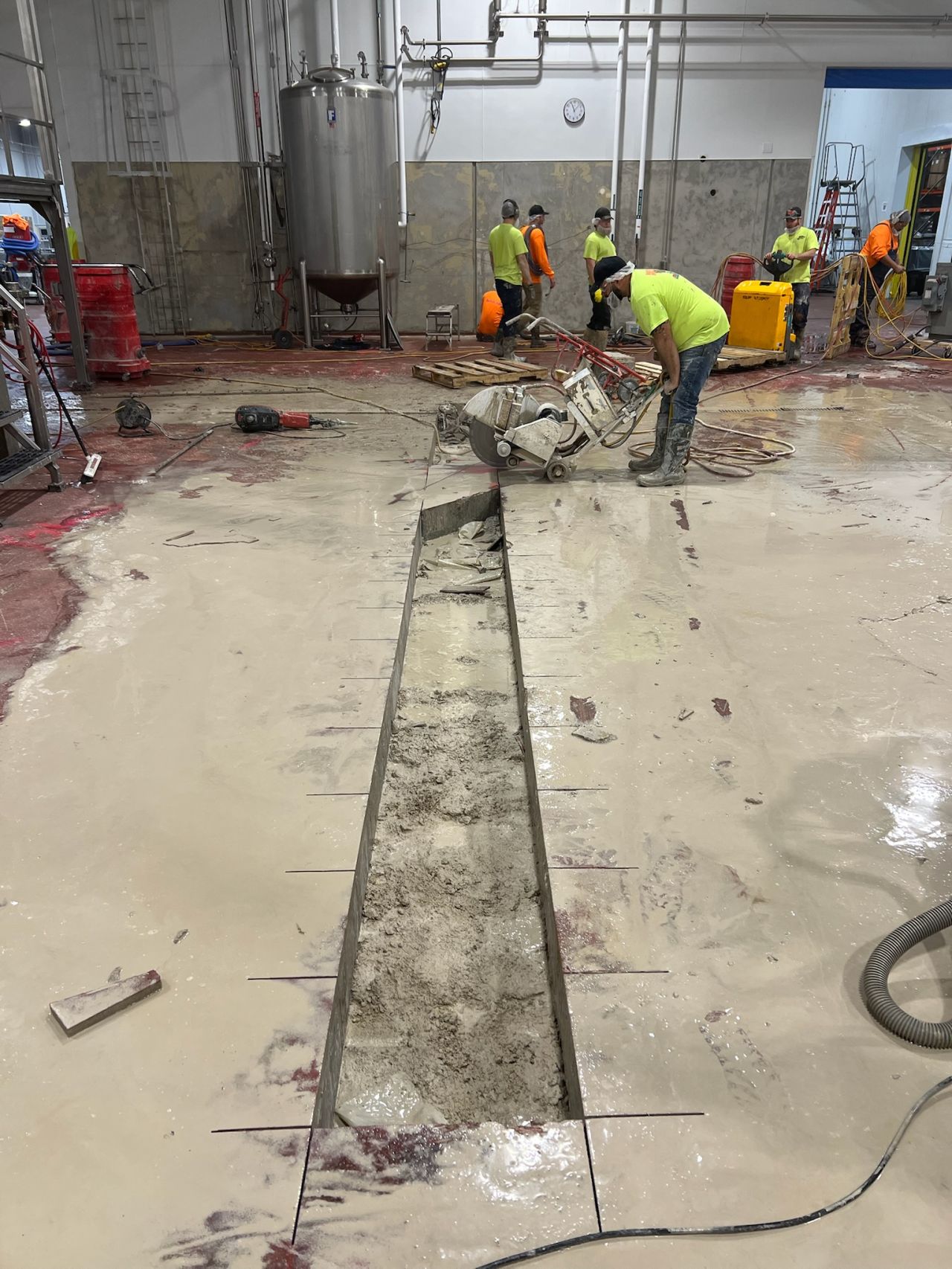 Crew cutting trench for new drain line installation in food processing production room