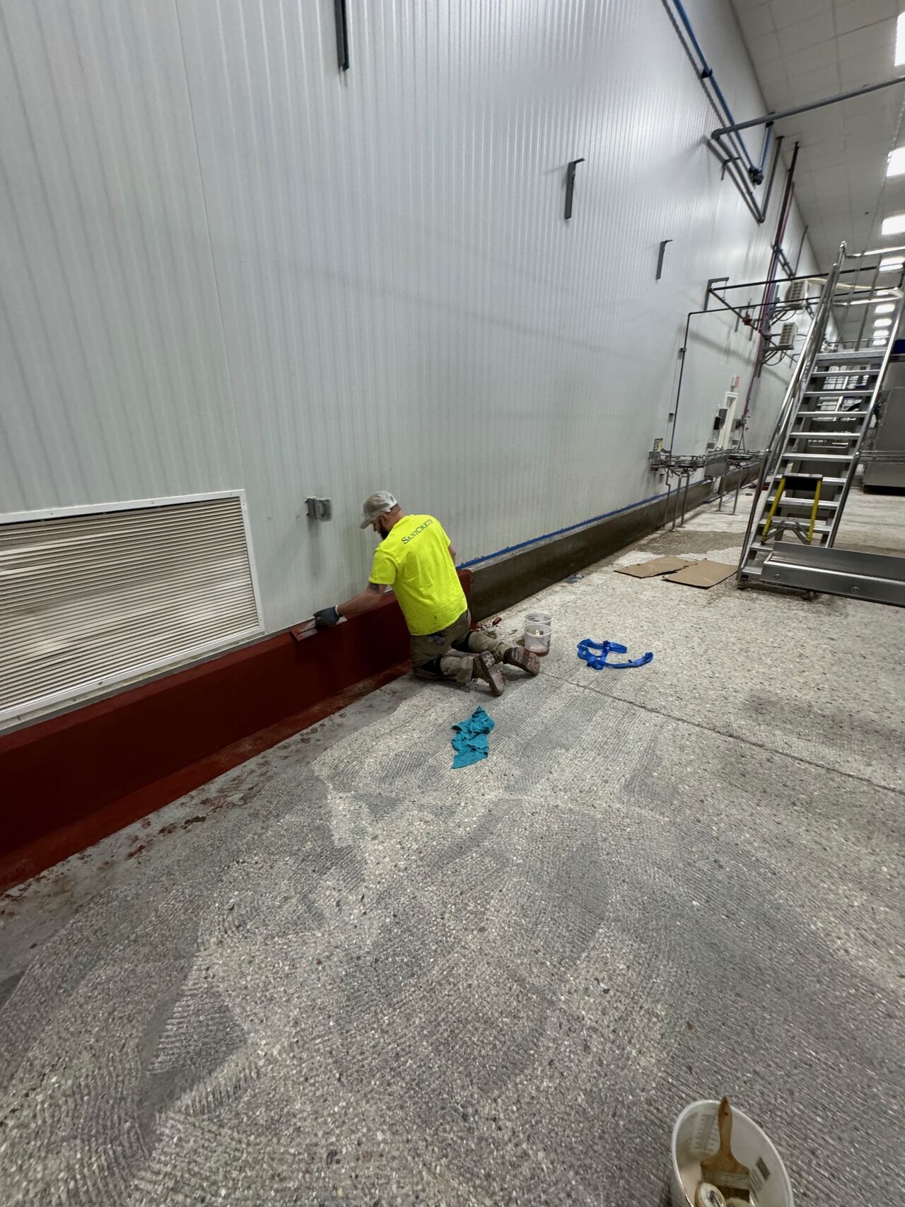SaniCrete crew member hand-troweling VR curbing along wall in food processing facility
