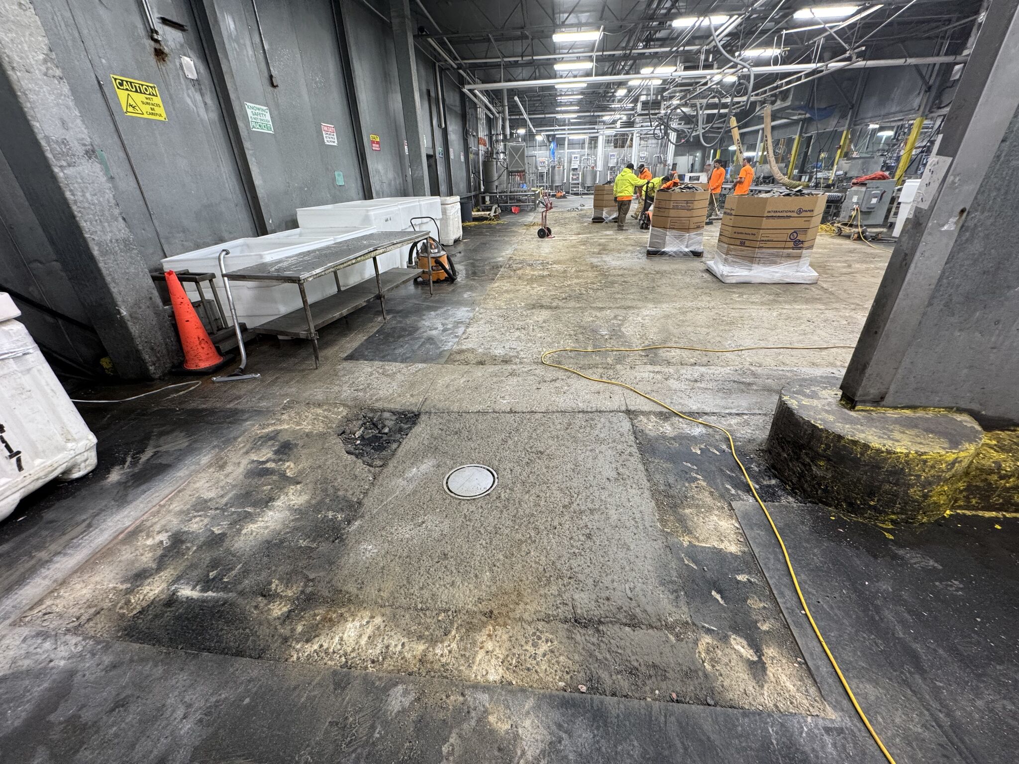 Poultry processing facility floor before replacement — worn, damaged dark surface with drain and stainless steel equipment