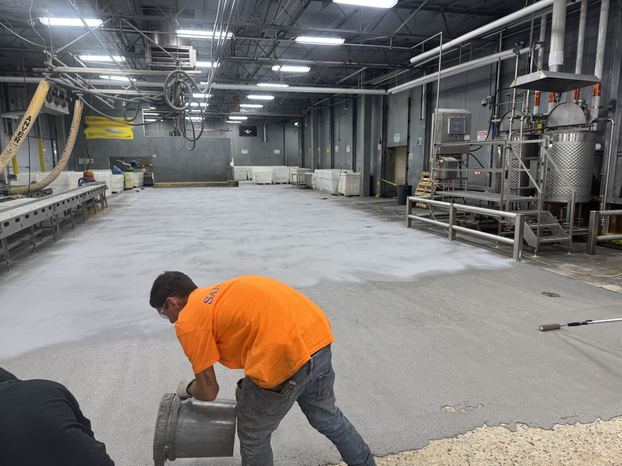 SaniCrete crew member in orange shirt pouring and spreading SaniCrete STX cementitious urethane