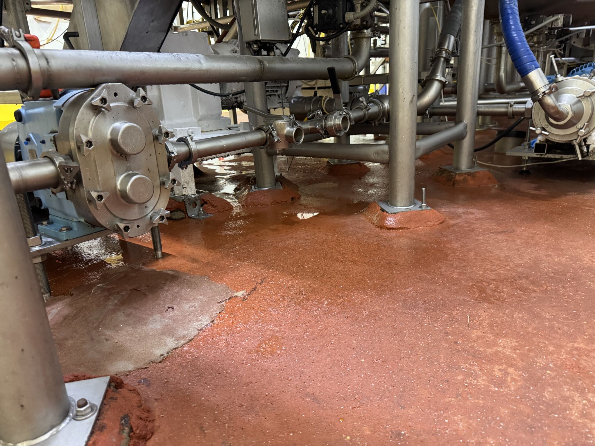 Before — severely delaminated red-brown floor with bare concrete exposed under processing equipment