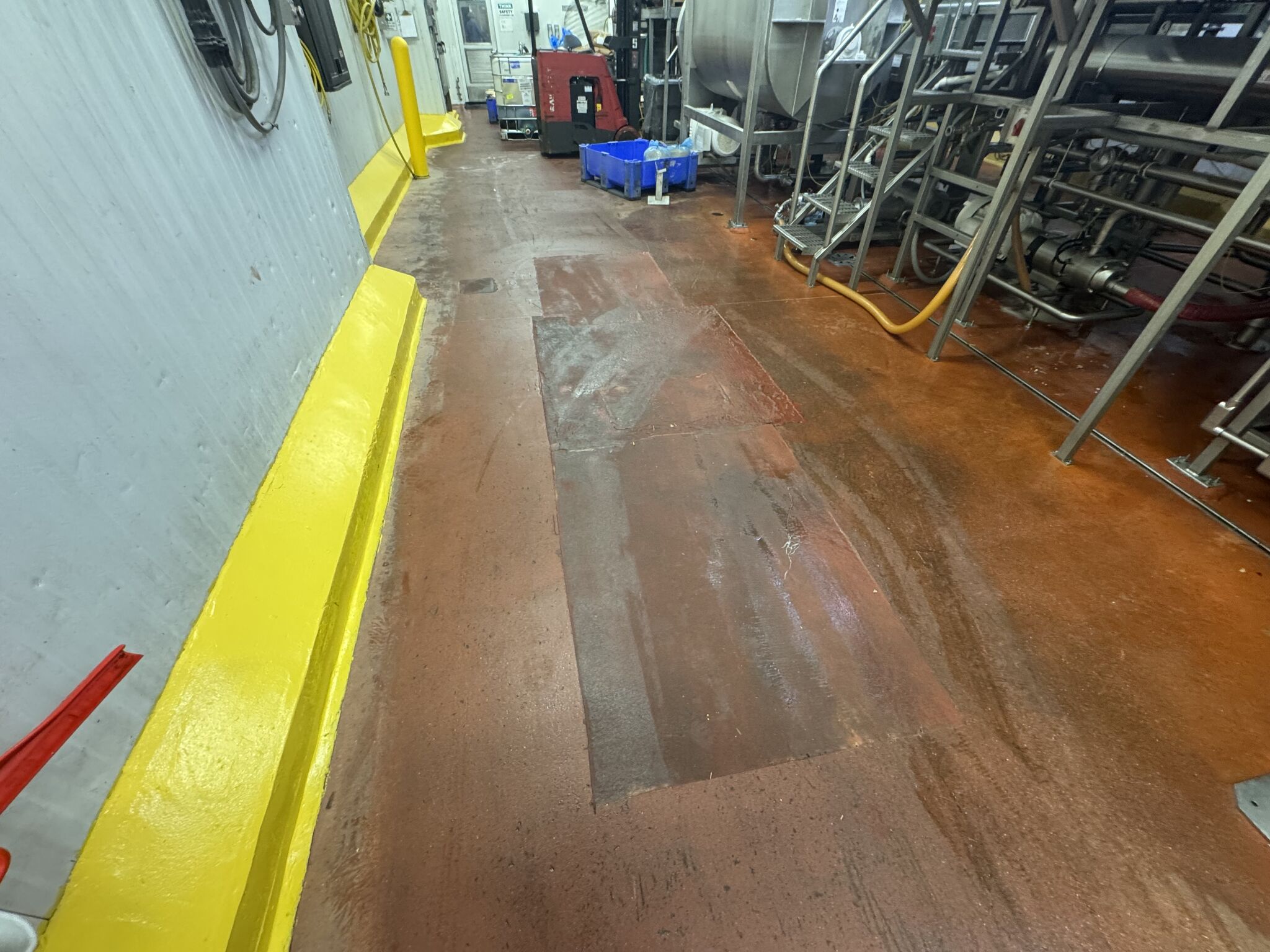 Before — worn floor with patched areas, yellow curbing, and heavy equipment traffic damage