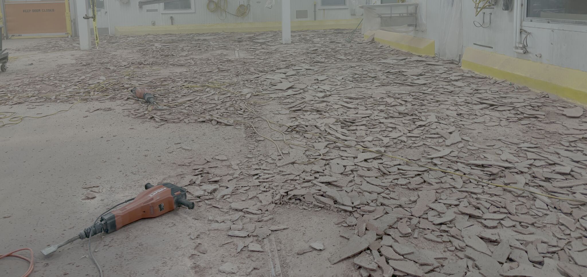 Delaminated production floor being demolished with jackhammer — chunks of failed coating covering the surface