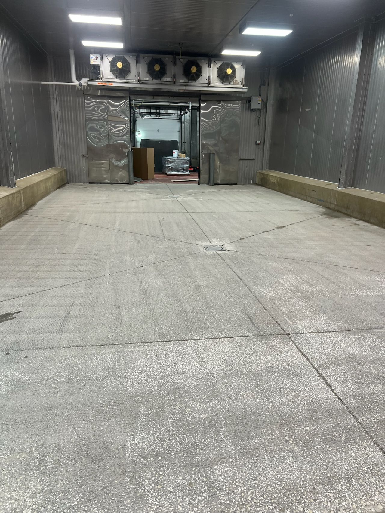 Cold storage room after surface profiling — clean concrete with center drain and evaporator fans